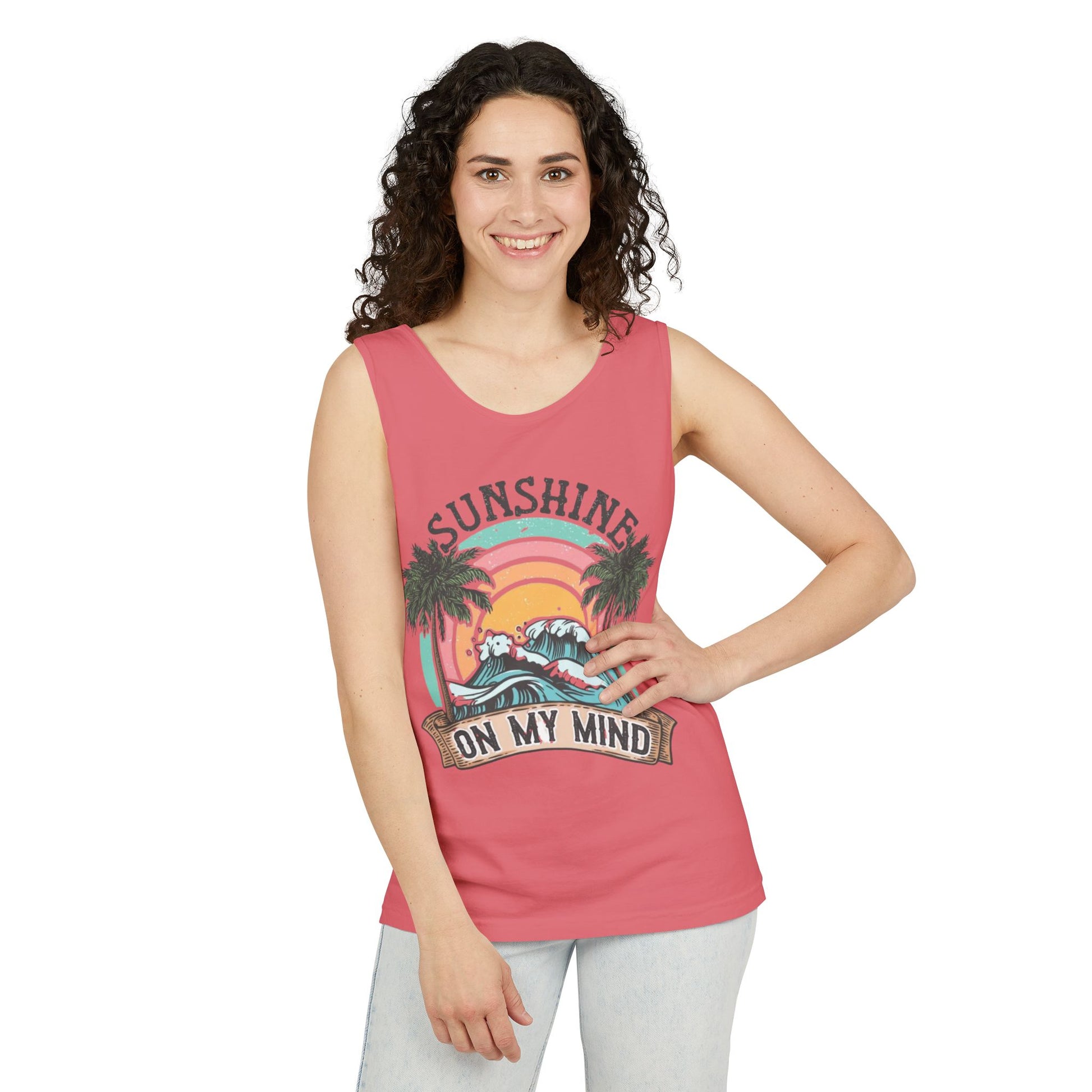 A woman with curly hair is smiling and posing in a pink tank top with a graphic design featuring palm trees and a sunset.