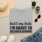 a gray t-shirt with the text "hold my halo, I'm about to do unto others" printed on it, along with a pair of jeans, sunglasses, a straw hat, and a pair of white sneakers.