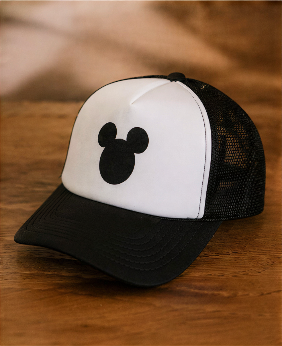 A black and white baseball cap with a Mickey Mouse logo on it, placed on a wooden surface.