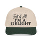 A beige baseball cap with a green brim, displaying the text "First of All I'm a Delight" in black lettering.