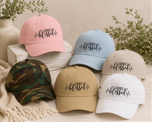 A collection of colorful baseball caps with the text "Simply Blessed" printed on them, displayed on a wooden surface with some greenery in the background.