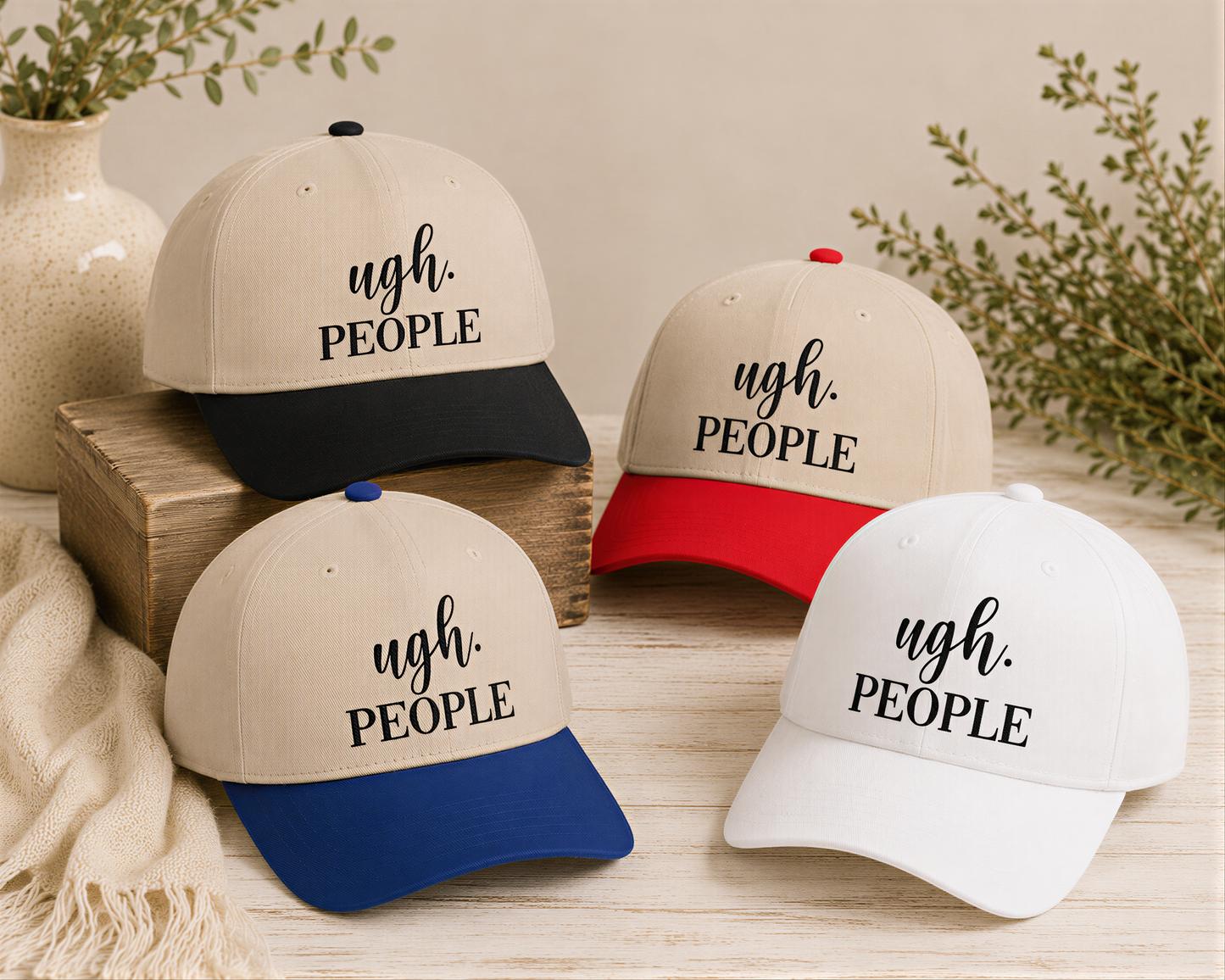 four baseball caps with the text "ugh. PEOPLE" printed on them, arranged on a wooden surface.
