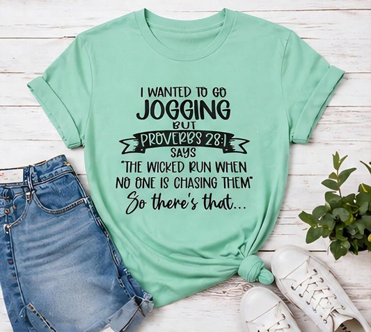 A green t-shirt with a humorous text printed on it, along with a pair of jeans and white sneakers, all laid out on a wooden surface.
