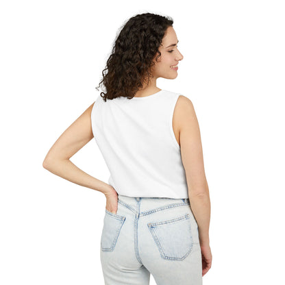 A woman with curly hair is smiling and looking to her left, wearing a white sleeveless top and light blue jeans.