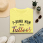 a yellow t-shirt with the text "F-BOMB MOM WITH TATToos" printed on it, along with a pair of sunglasses, a hat, and some plants.