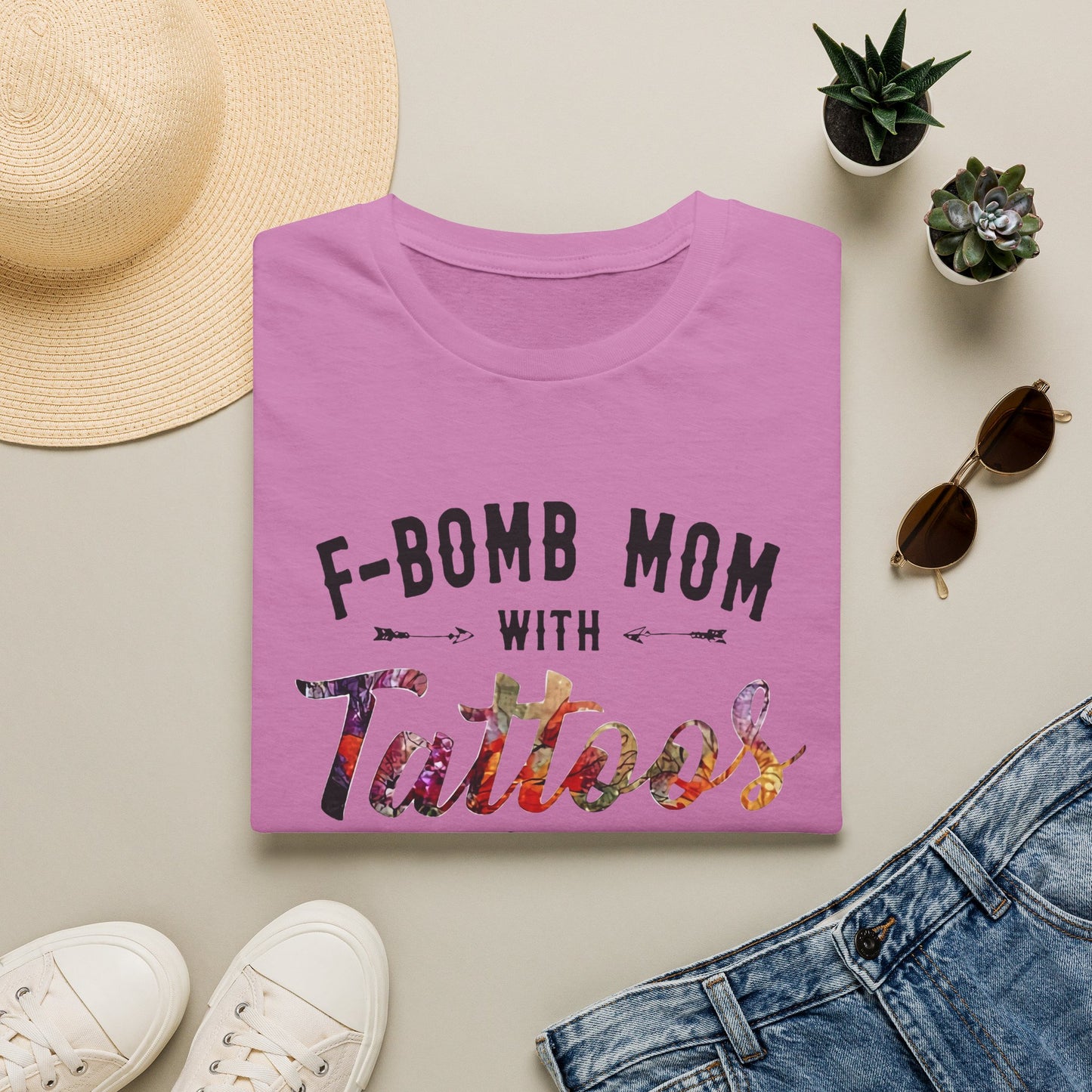 a pink t-shirt with the text "F-BOMB MOM WITH Tattoos" printed on it, along with a pair of jeans, sunglasses, and a straw hat.
