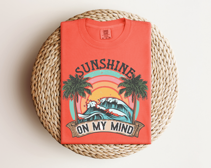 a red t-shirt with a graphic design depicting a sunset and palm trees, along with the text "SUNSHINE ON MY MIND".