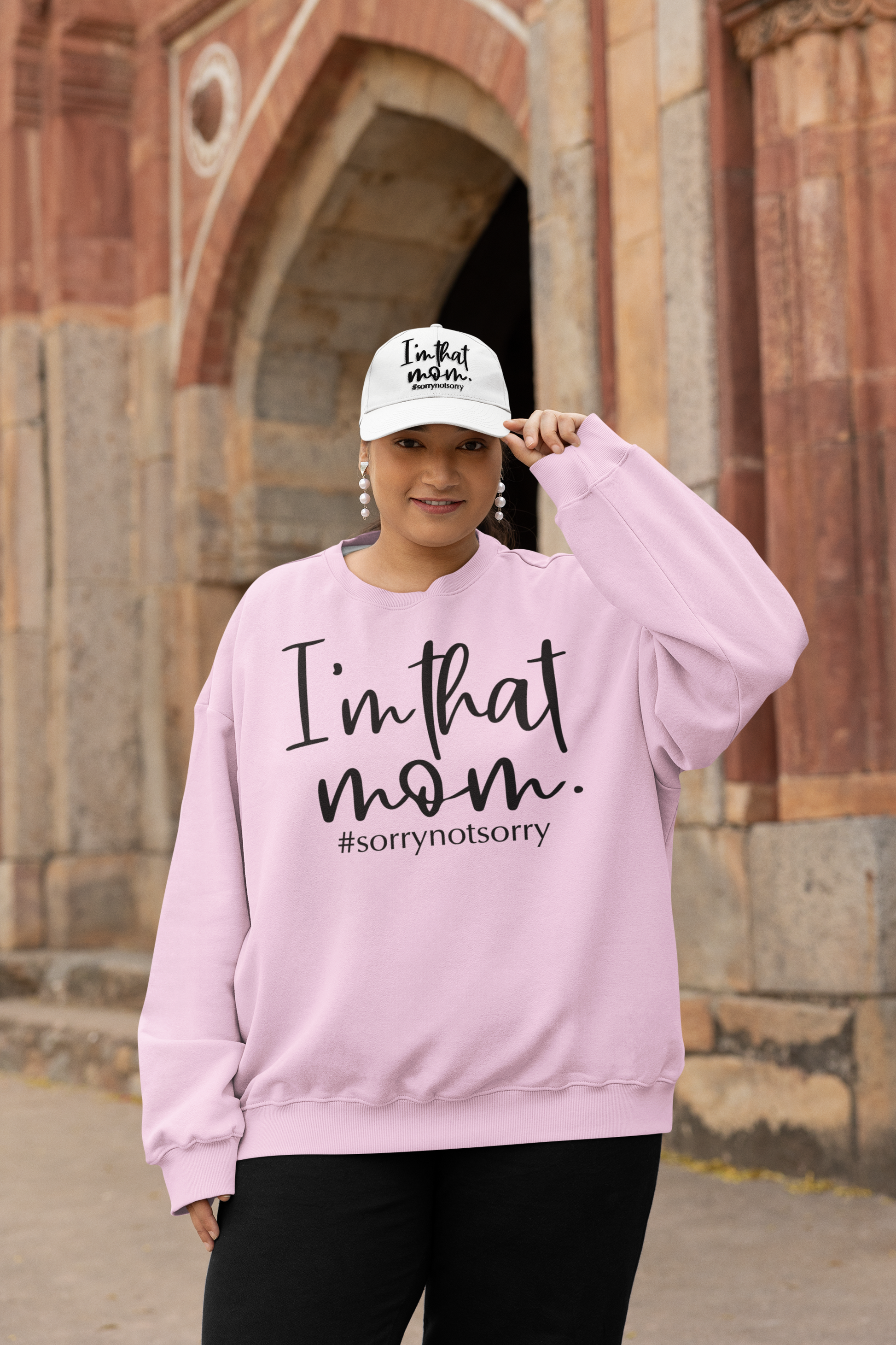 A woman wearing a pink sweatshirt with the text "I'm that mom. #sorroynotsorry" stands in front of a brick building.